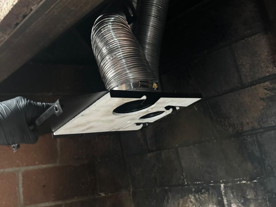 Gloved hand fitting an adapter plate connected to two stainless steel flexible liners inside a fireplace