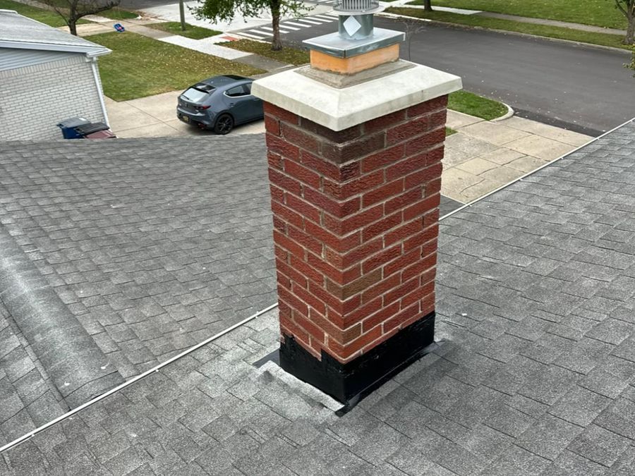 Red brick chimney with a white concrete crown and a stainless steel cap on a gray shingle roof