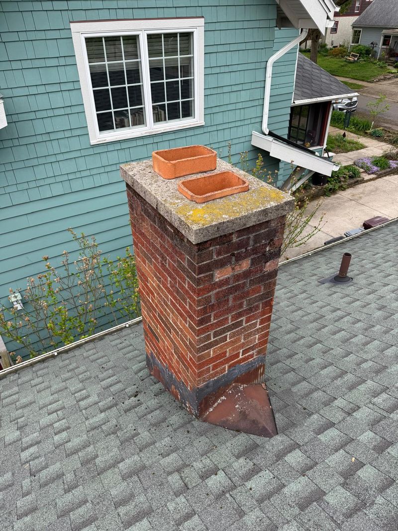 Brick chimney with a lichen-covered crown, two clay flue tiles and rusted flashing
